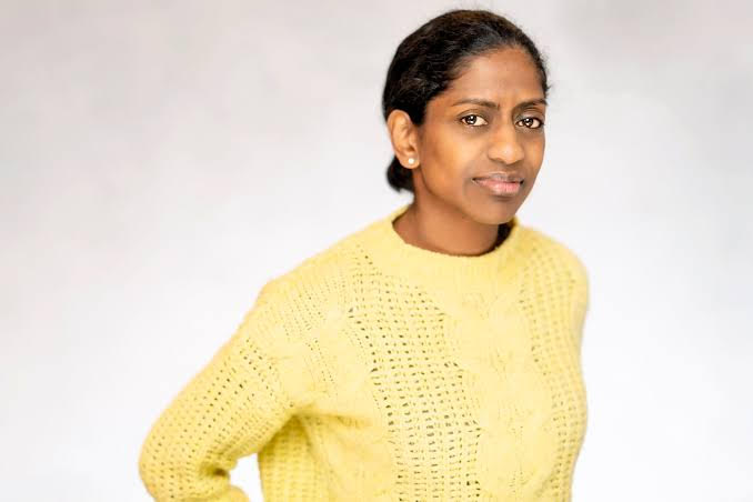 Nadia is British South Asian with dark skin. She has dark hair and wears a yellow jumper.